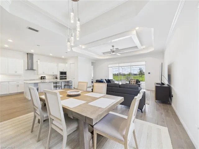 Dining space featuring a tray ceiling, light wood-style floors, a ceiling fan, ornamental molding, and recessed lighting