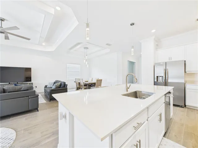 Kitchen featuring wood finish floors, crown molding, white cabinetry, stainless steel appliances, and hanging light fixtures