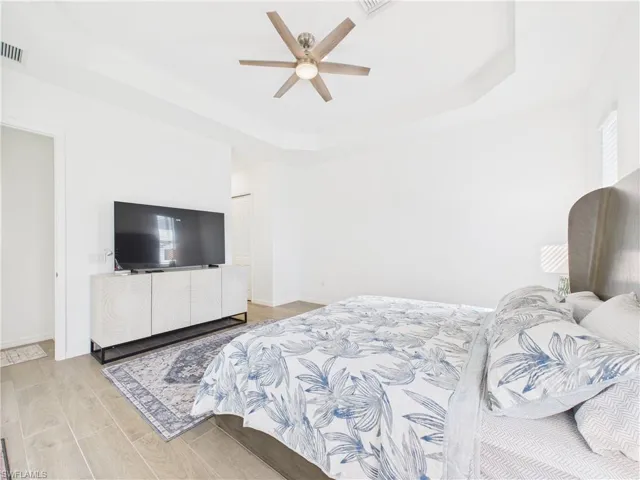 Bedroom with a tray ceiling, light wood-type flooring, and a ceiling fan
