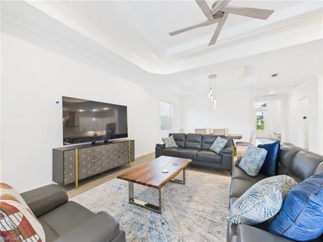 Living room with a tray ceiling, healthy amount of natural light, wood finished floors, and crown molding