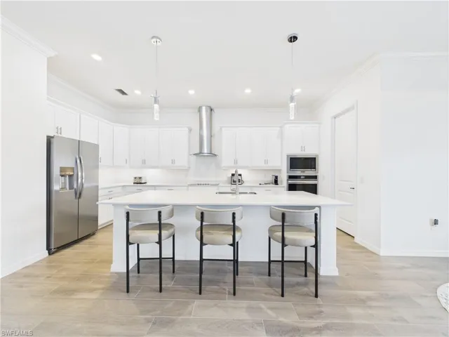 Kitchen featuring stainless steel appliances, pendant lighting, white cabinetry, a kitchen bar, and a kitchen island with sink