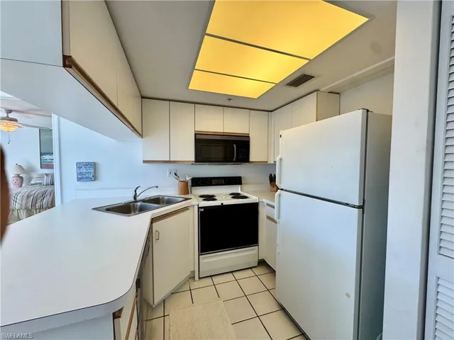 Kitchen with white appliances, light countertops, white cabinets, a peninsula, and light tile  floors