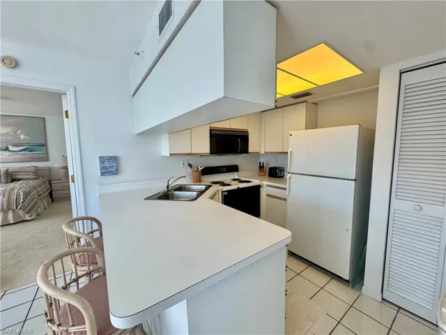 Kitchen with white appliances, light countertops, a peninsula, a kitchen breakfast bar, and light tile flooring