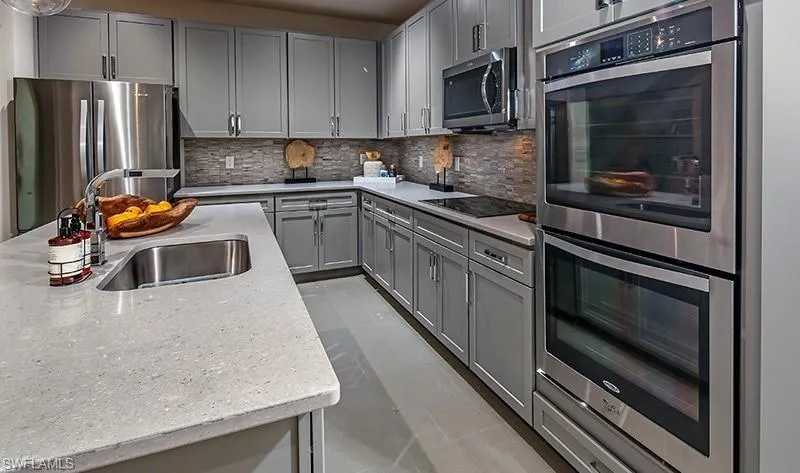 Kitchen with stainless steel appliances, decorative backsplash, light stone countertops, and gray cabinetry