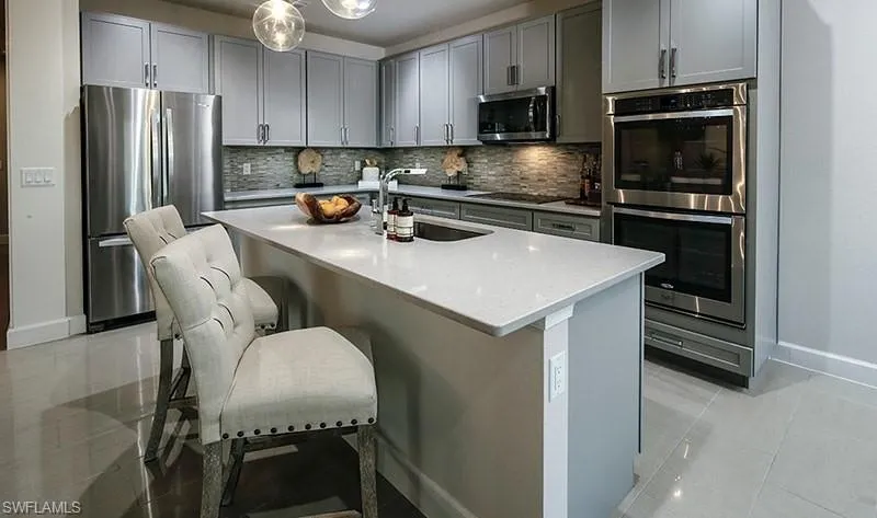 Kitchen with stainless steel appliances, backsplash, light stone countertops, an island with sink, and light tile patterned floors