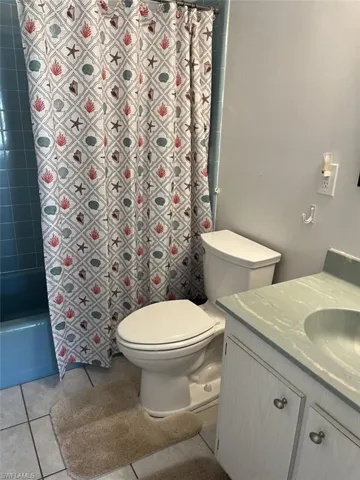 Full bathroom with shower / bath combination with curtain, vanity, tile patterned flooring, and toilet
