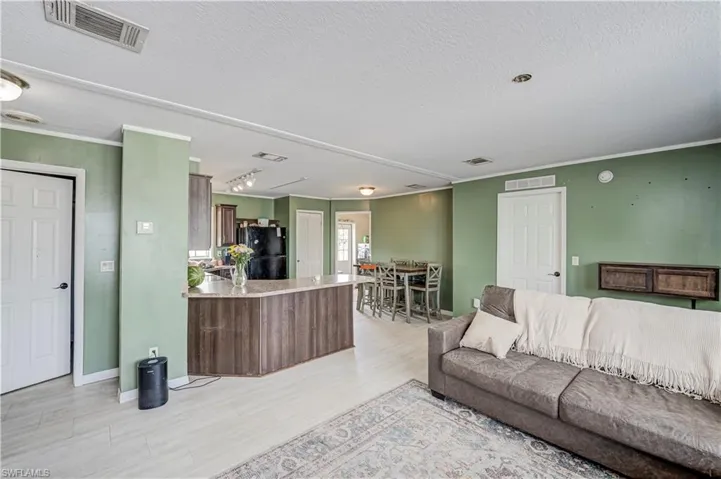 Open-concept living area featuring light wood-finish flooring, recessed lighting, and crown molding