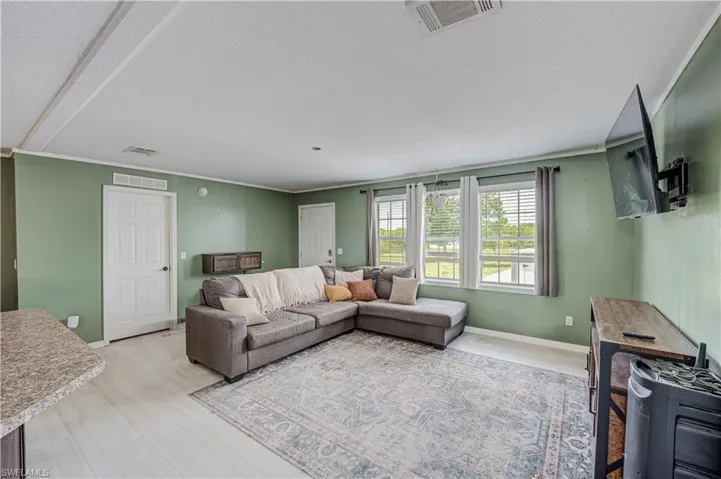 Expansive living area featuring light-toned flooring, three large windows with white blinds, and a built-in floating cabinet