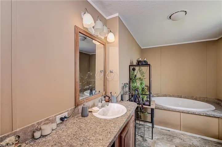 Bathroom featuring a built-in soaking tub with a stone-finish surround, a single vanity with an integrated sink, a wood-framed mirror, and overhead lighting