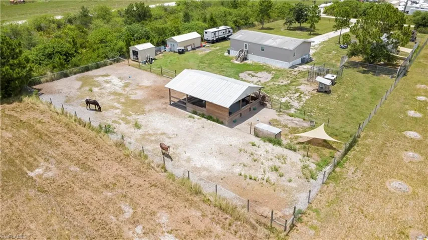 Expansive fenced property featuring a large open-air structure with a metal roof, multiple storage sheds, a manufactured home, and mature trees