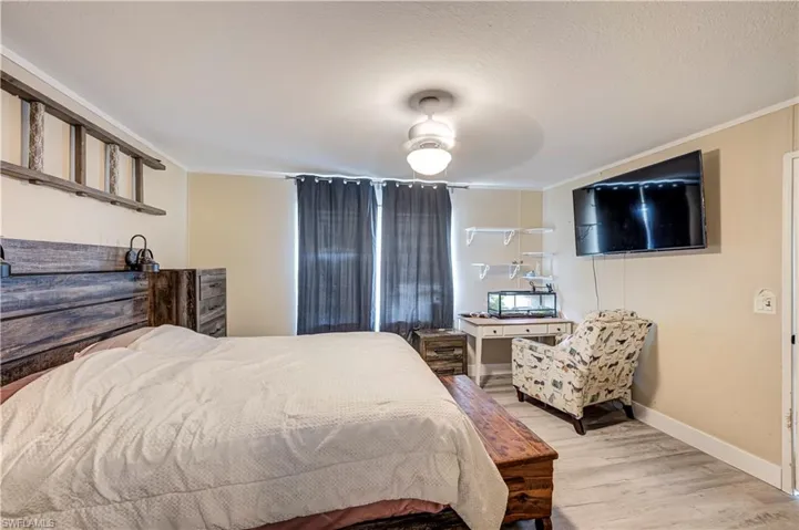 Spacious bedroom featuring light wood-finish flooring, a ceiling-mounted light fixture, and crown molding