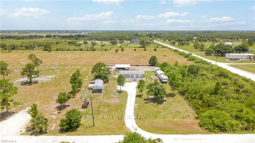Expansive rural property featuring a main residence, detached outbuilding, mature trees, and a long gravel driveway