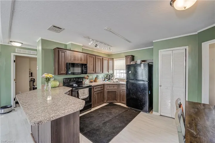 Kitchen featuring wood-finish cabinetry, black appliances, track lighting, and a breakfast bar with a speckled countertop