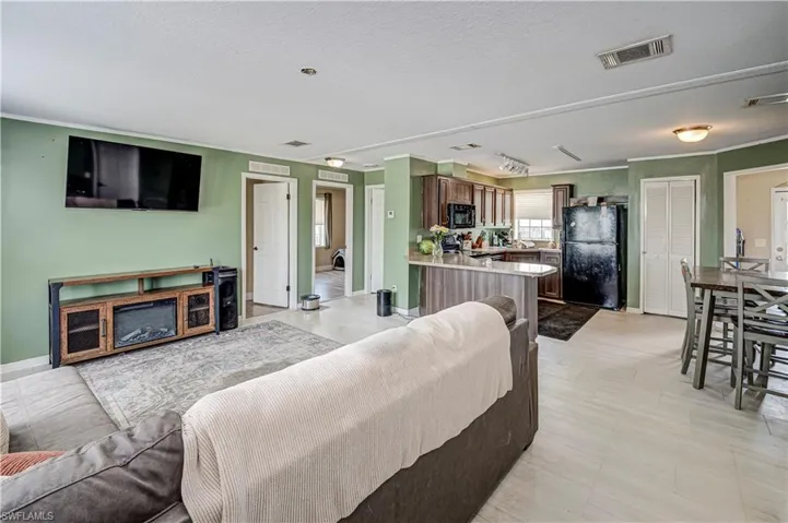 Open-concept living area featuring light-toned flooring, a kitchen with wood cabinetry and a peninsula, and a dining area with a high-top table