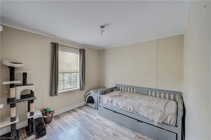 Room featuring wood-finish flooring, a window with horizontal blinds and drapes, and light-toned wall paneling