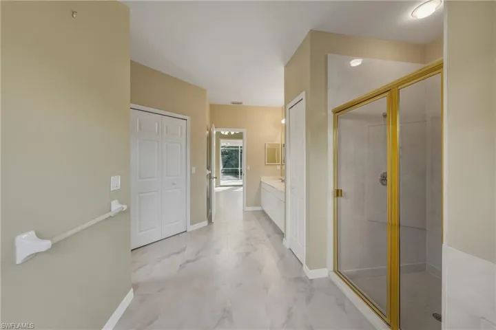 Full bath featuring vanity, a stall shower, a closet, and light marble finish flooring