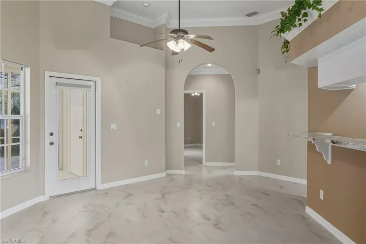 Spare room with light marble finish floors, ornamental molding, ceiling fan, arched walkways, and a high ceiling