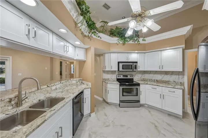Kitchen with stainless steel appliances, white cabinets, light stone countertops, ceiling fan, and ornamental molding