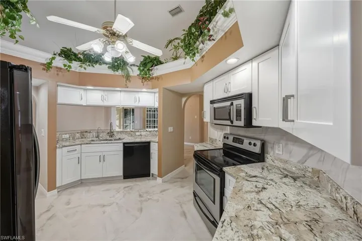 Kitchen with black appliances, light stone counters, white cabinetry, crown molding, and light marble finish floors