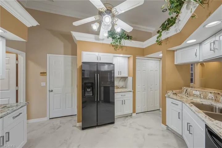 Kitchen with crown molding, light stone countertops, white cabinetry, refrigerator with ice dispenser, and light marble finish floors