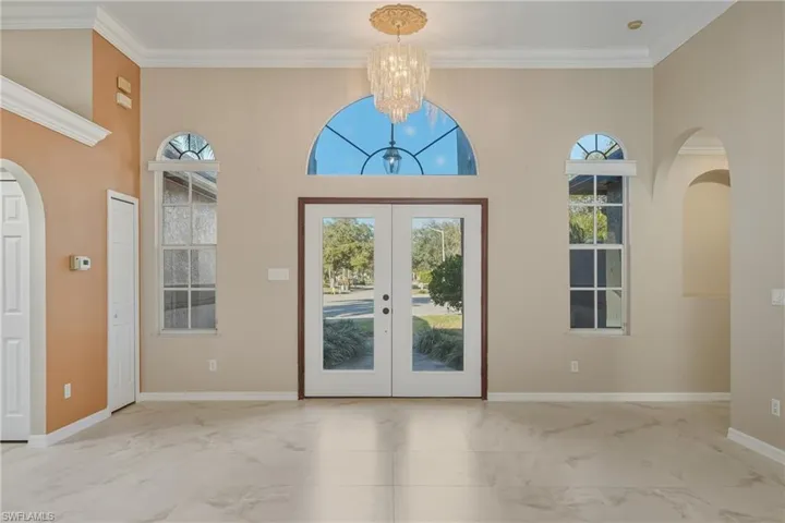 Doorway featuring arched walkways, ornamental molding, french doors, hanging lights, and a high ceiling