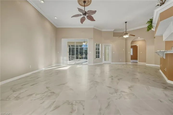 Unfurnished living room featuring crown molding, arched walkways, and a ceiling fan