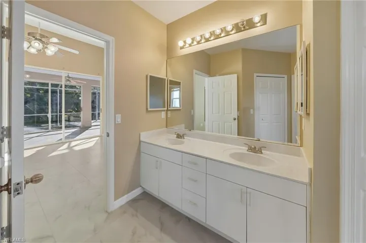 Bathroom with double vanity, light marble finish floors, and ceiling fan