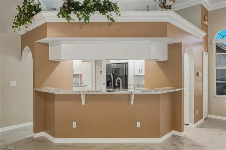 Kitchen featuring arched walkways, light stone countertops, stainless steel fridge, white cabinetry, and crown molding