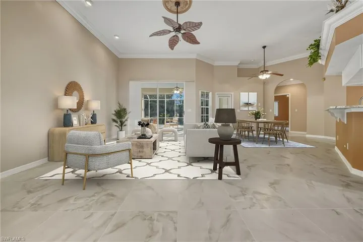 Living area featuring crown molding, arched walkways, a ceiling fan, a high ceiling, and light marble finish flooring