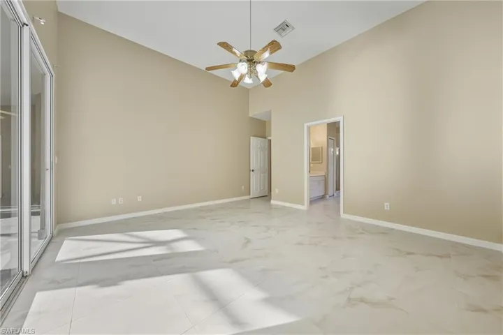 Unfurnished bedroom with a high ceiling, light marble finish floors, access to exterior, ensuite bath, and a ceiling fan
