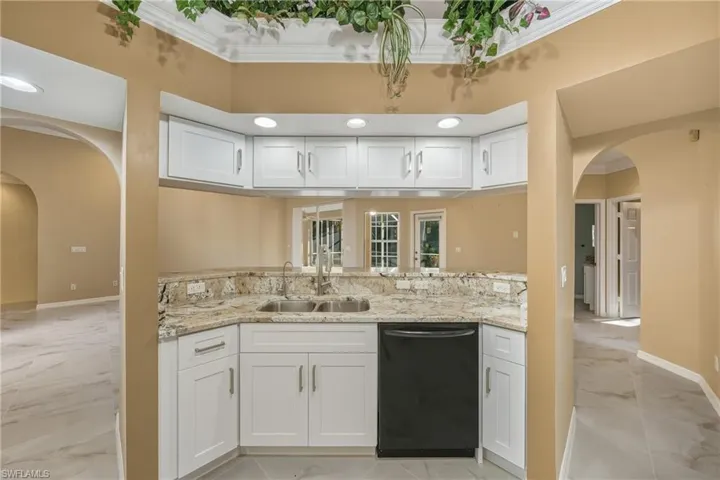 Kitchen with arched walkways, white cabinetry, light stone countertops, light marble finish floors, and crown molding
