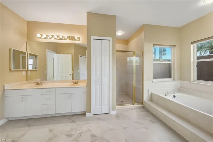 Full bath featuring a closet, a bath, double vanity, a shower stall, and light marble finish floors
