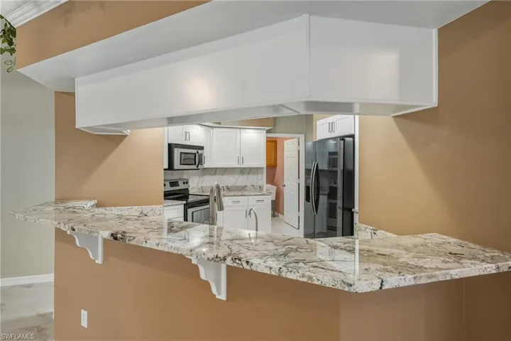Kitchen featuring stainless steel appliances, decorative backsplash, a peninsula, and white cabinetry