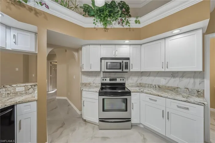 Kitchen featuring stainless steel appliances, white cabinets, light marble finish floors, light stone counters, and arched walkways