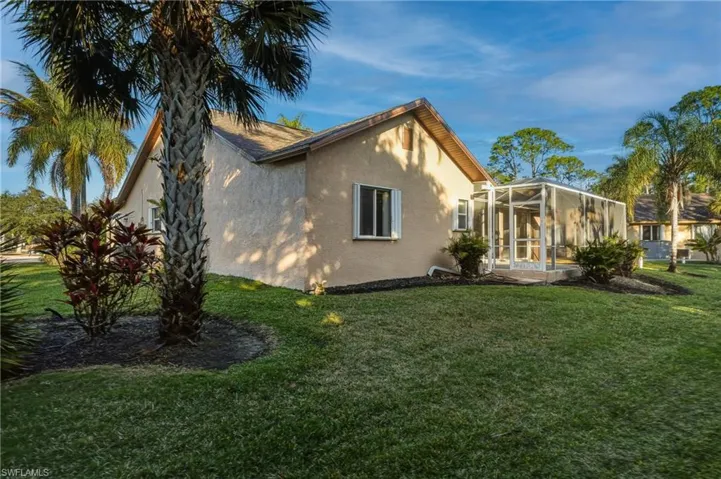 View of side of home with a sunroom, glass enclosure, stucco siding, and a yard