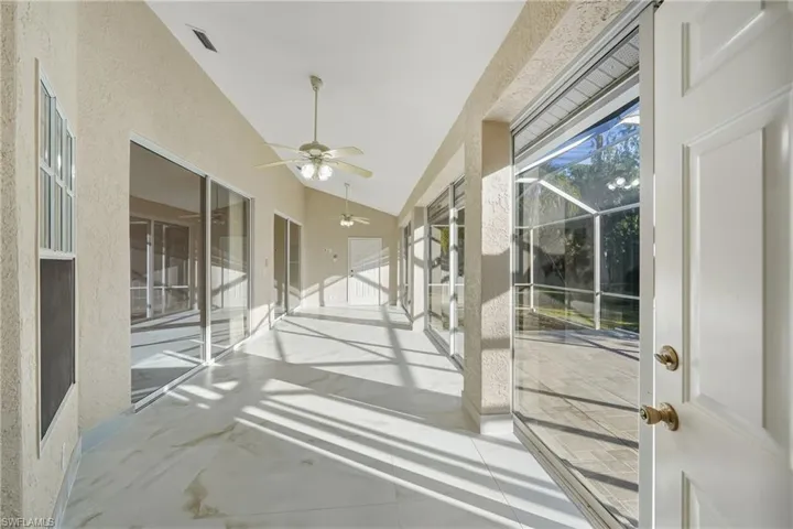 Unfurnished sunroom with a ceiling fan, a patio, and vaulted ceiling