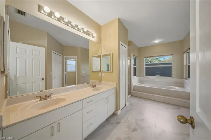 Full bathroom with double vanity, a bath, and light marble finish floors