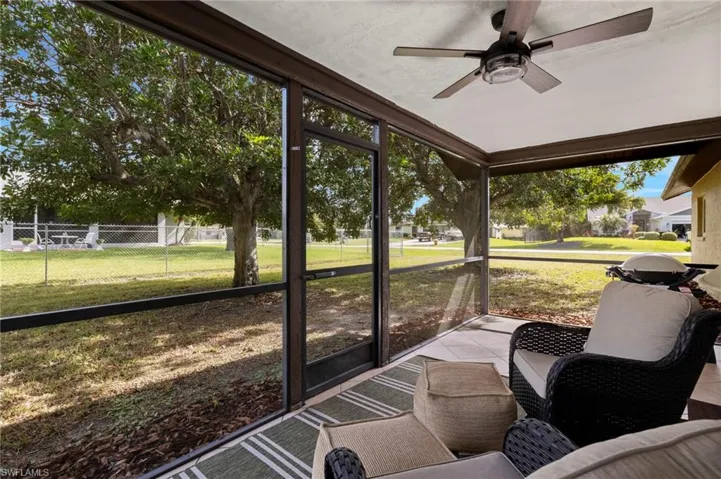 Step onto the screened patio and take in the peaceful backyard view, where lush grass and a towering tree create a serene natural retreat.