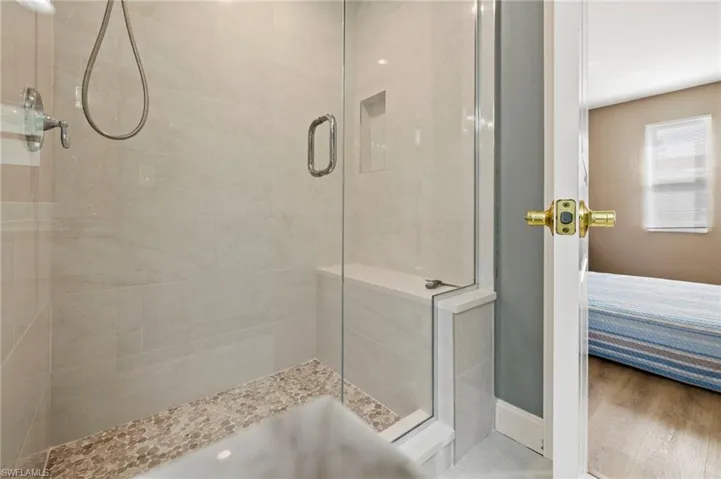 The primary bathroom includes luxury vinyl flooring, tile that goes from floor to ceiling, a bench, and multiple shower heads.