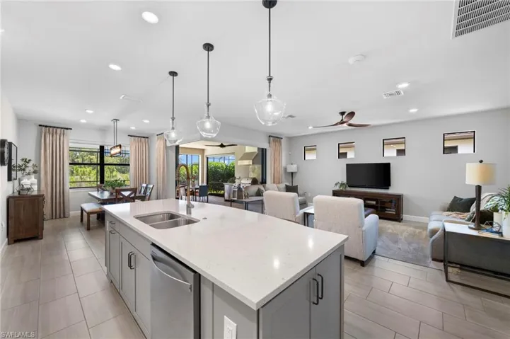 Kitchen featuring open floor plan, light stone countertops, stainless steel dishwasher, gray cabinetry, and pendant lighting