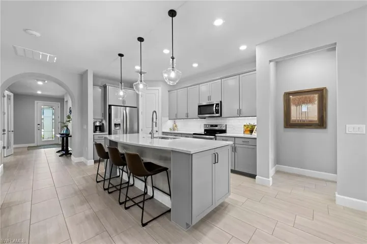 Kitchen featuring arched walkways, a kitchen breakfast bar, appliances with stainless steel finishes, an island with sink, and decorative backsplash