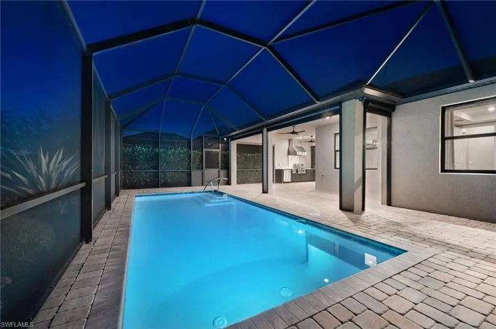 Pool at twilight with an outdoor kitchen, an outdoor pool, a lanai, and screen enclosure