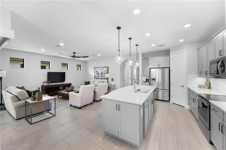 Kitchen featuring stainless steel appliances, backsplash, decorative light fixtures, open floor plan, and a ceiling fan