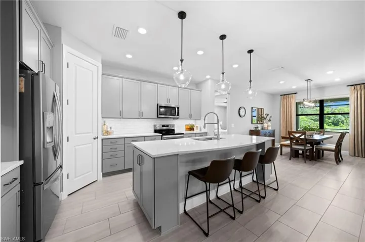 Kitchen featuring a center island with sink, decorative backsplash, a kitchen bar, appliances with stainless steel finishes, and decorative light fixtures