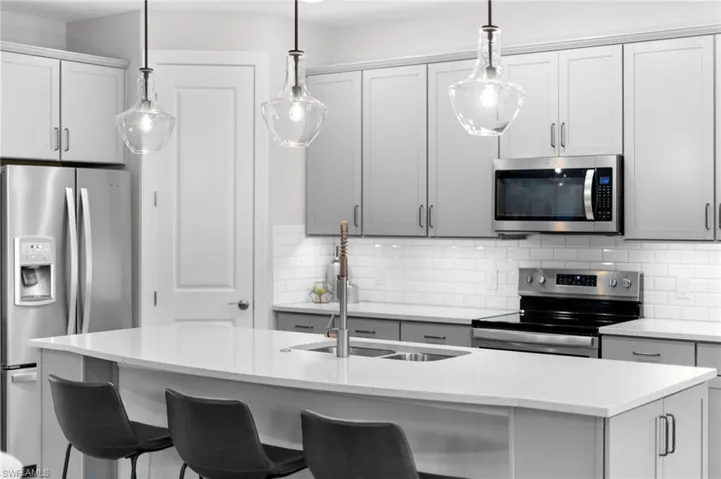 Kitchen with appliances with stainless steel finishes, tasteful backsplash, light stone countertops, a breakfast bar, and a center island with sink