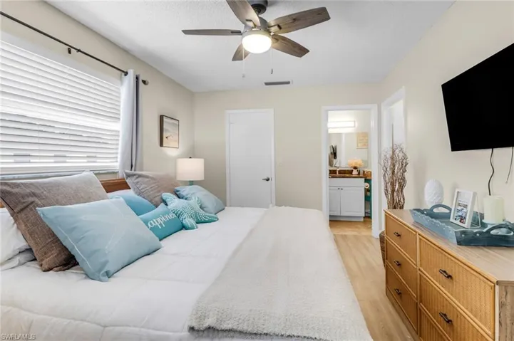 Bedroom with light wood-style flooring, ceiling fan, connected bathroom, and a textured ceiling