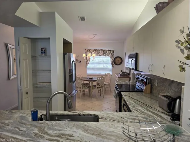 Kitchen featuring light tile patterned flooring, black appliances, hanging light fixtures, light stone countertops, and a chandelier