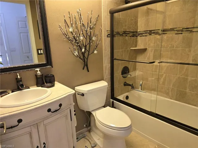 Full bath featuring bath / shower combo with glass door, vanity, and a textured wall