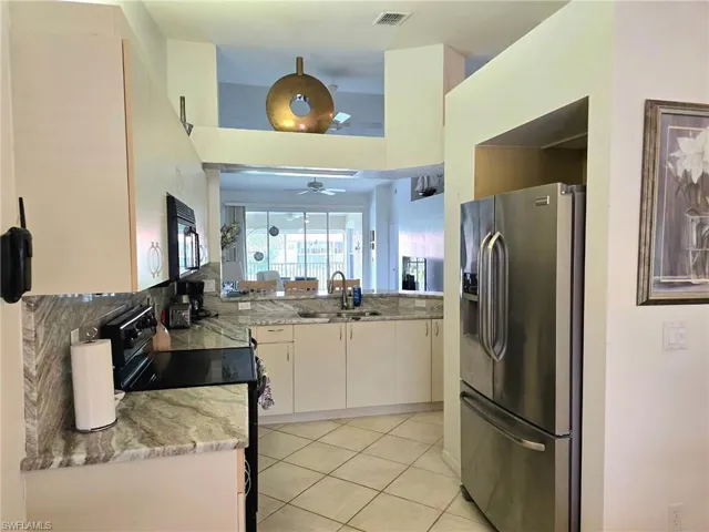 Kitchen featuring black appliances, light tile patterned floors, light stone countertops, tasteful backsplash, and white cabinets