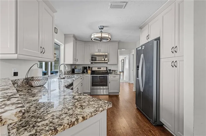Kitchen with white cabinetry, stainless steel appliances, sink, light stone countertops, and dark wood-type flooring